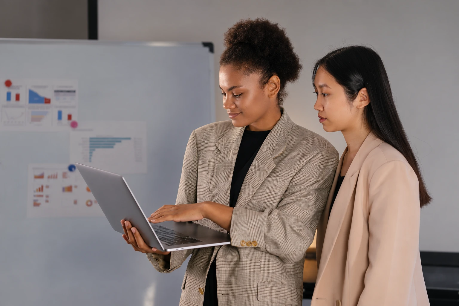 Two colleagues reviewing a laptop together beside a planning board.